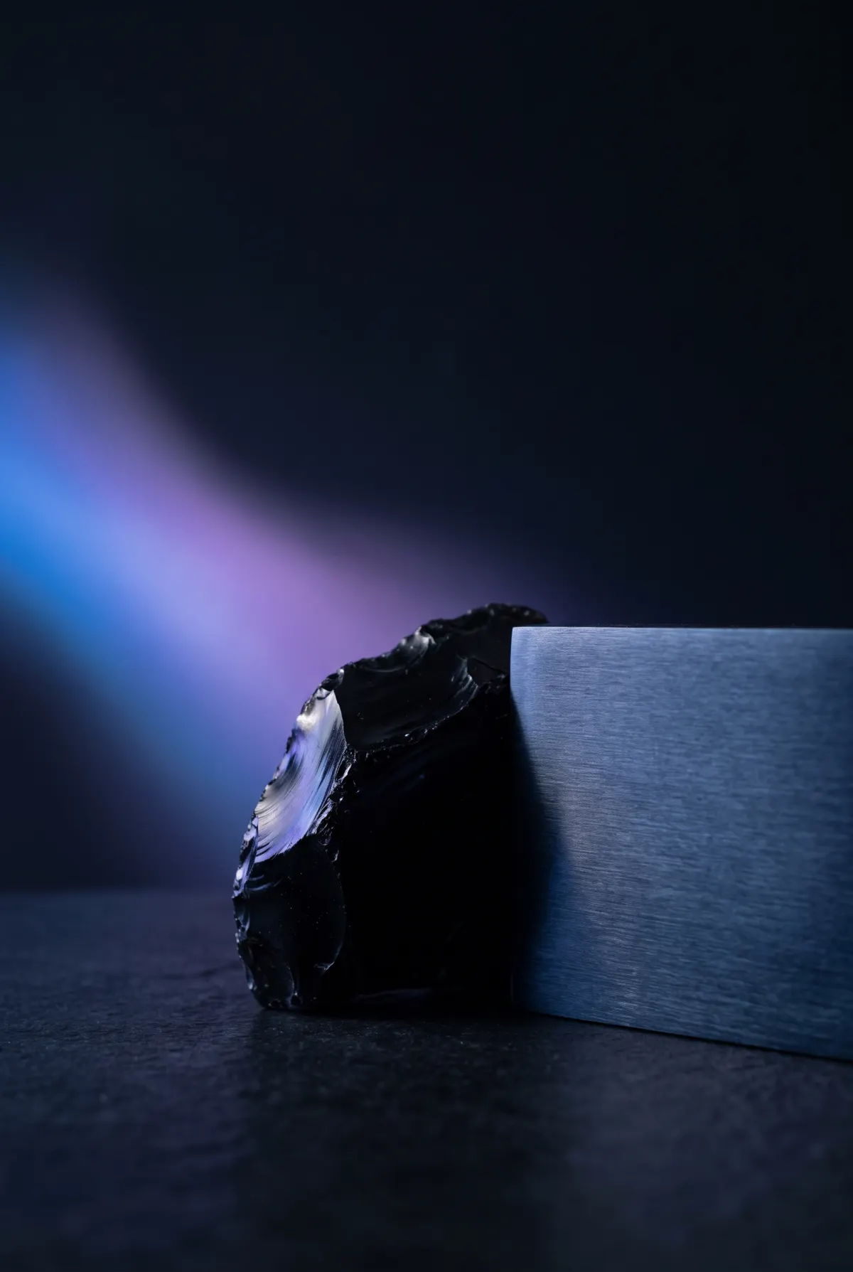 Obsidian and brushed metal lit by a soft blue and violet wash